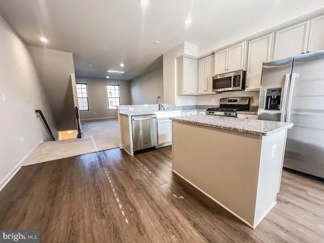 a kitchen with stainless steel appliances a refrigerator a stove a sink cabinets and wooden floor