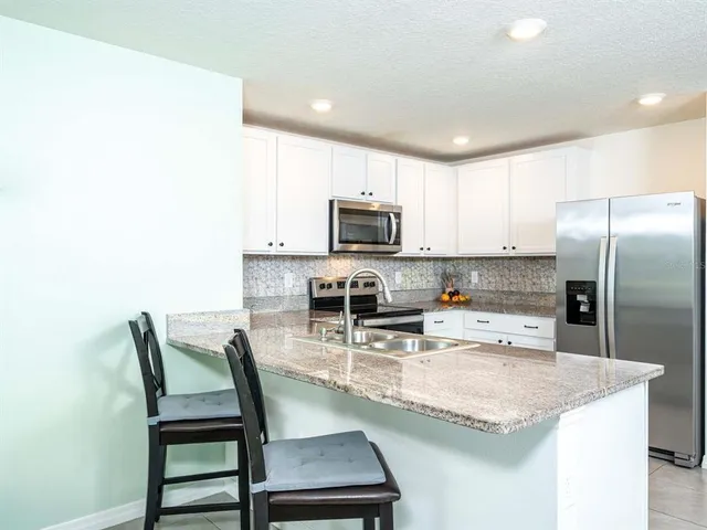 a kitchen with kitchen island granite countertop a table chairs microwave and refrigerator