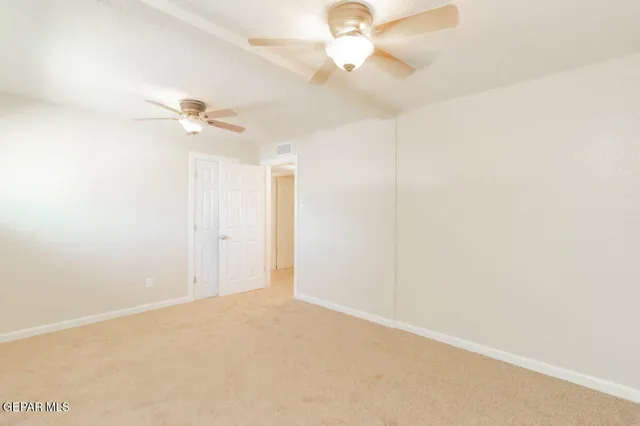 an empty room with a chandelier fan and windows