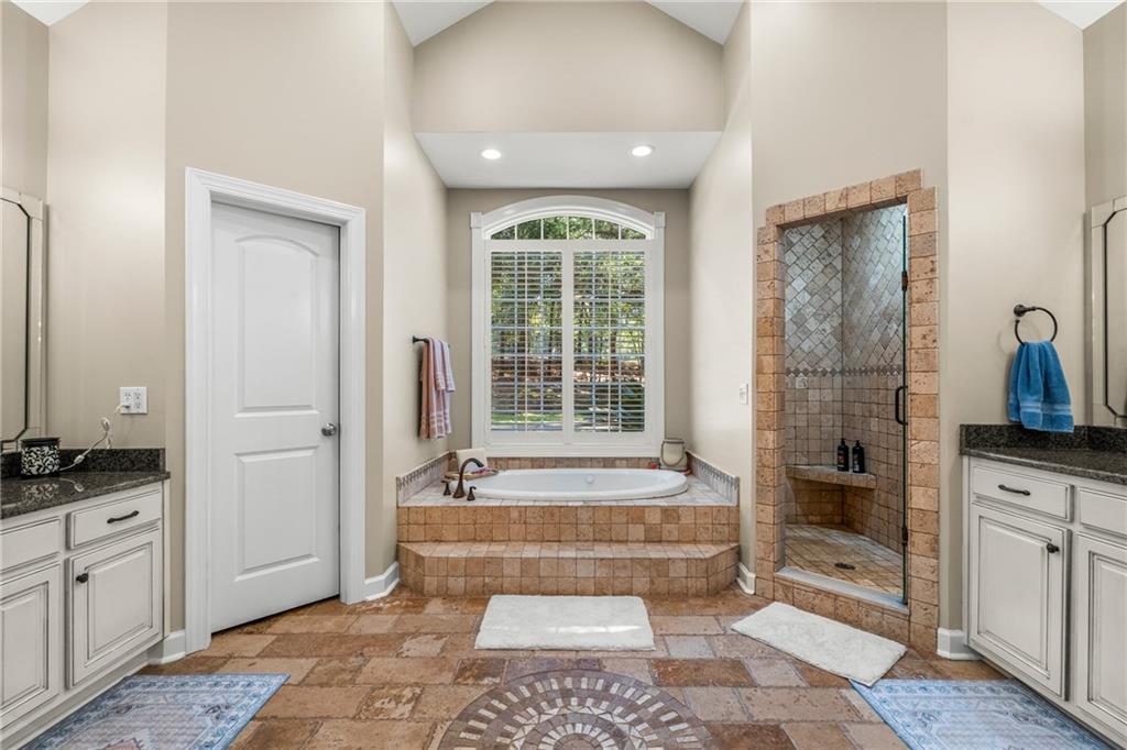 642 Nuckols Road Seale, AL 36875 - Photo 16 of 48 Vaulted ceiling, arched window with horizontal blinds, tiled walk-in shower with bench, built-in soaking tub, and dual vanity sinks with dark countertops