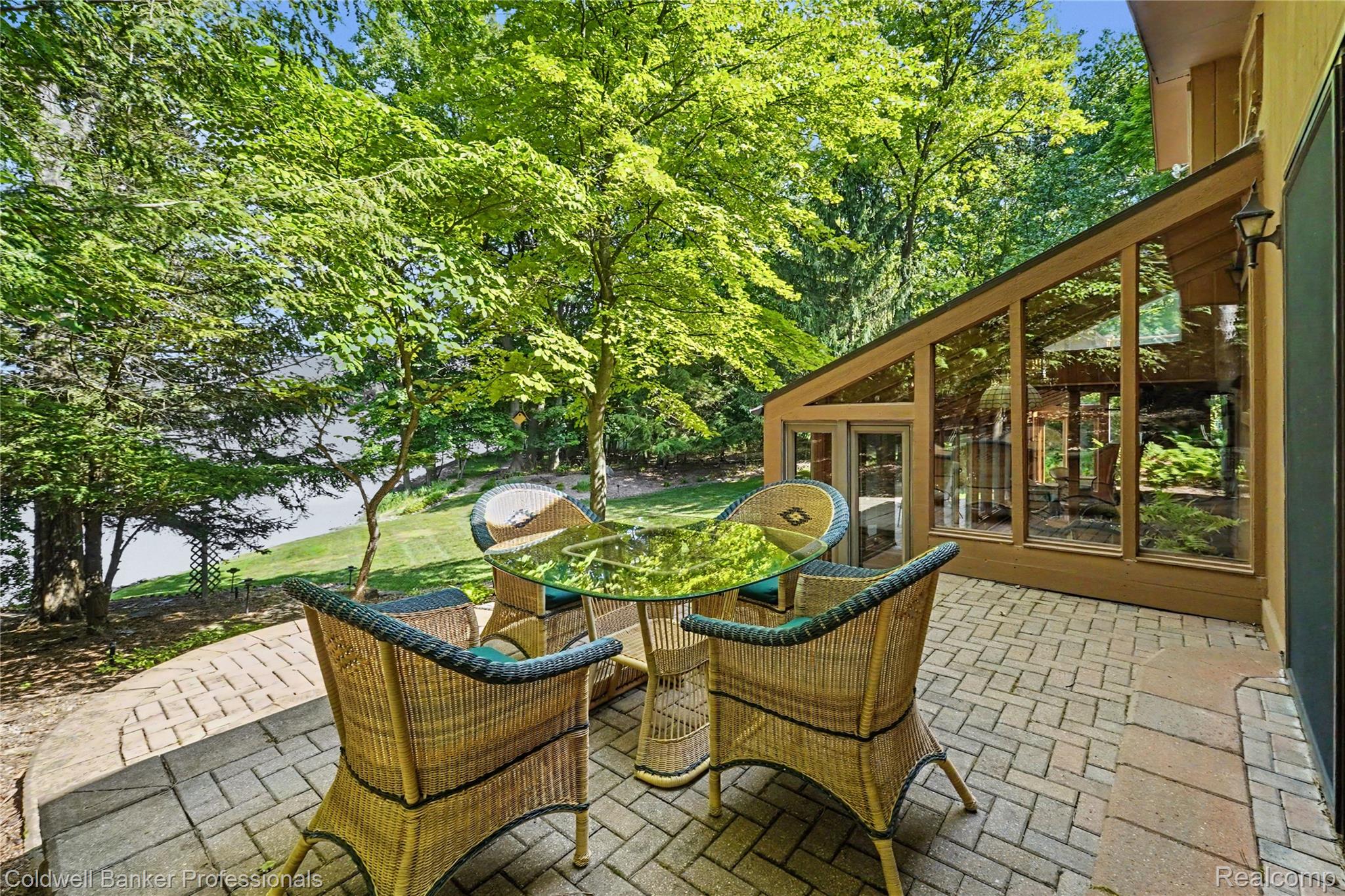 3583 Mitchell Road Metamora, MI 48455 - Photo 4 of 58 Paved patio with a curved stone border, featuring an adjacent sunroom with floor-to-ceiling windows and an exterior wall light fixture