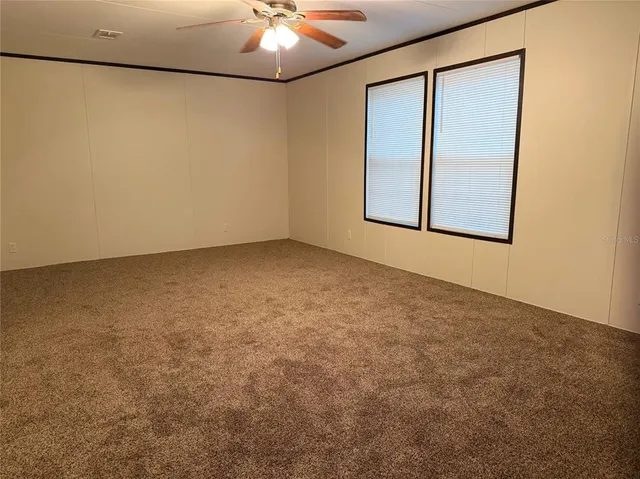 an empty room with a chandelier fan and windows