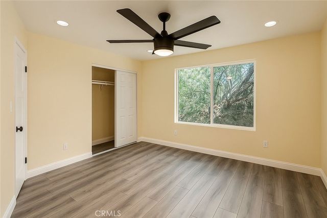 an empty room with wooden floor ceiling fan and windows