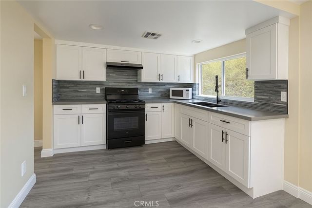 a kitchen with stainless steel appliances granite countertop a stove top oven a sink and white cabinets