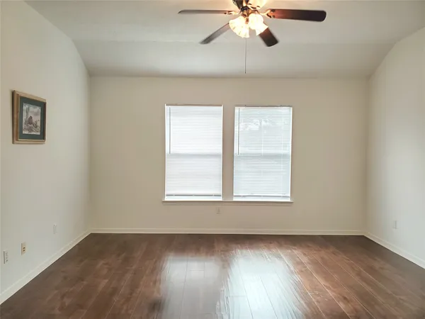 an empty room with wooden floor fan and windows