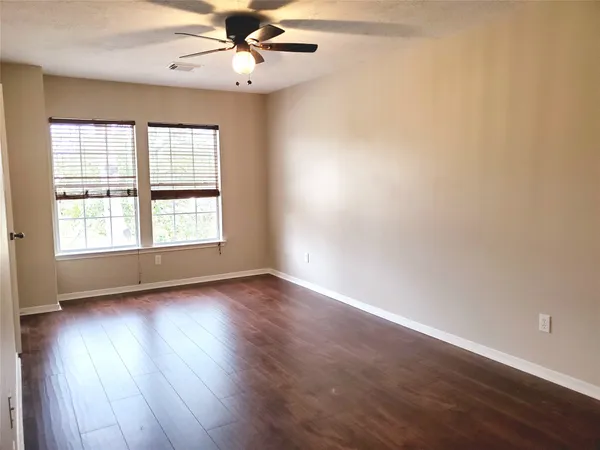 an empty room with wooden floor fan and windows