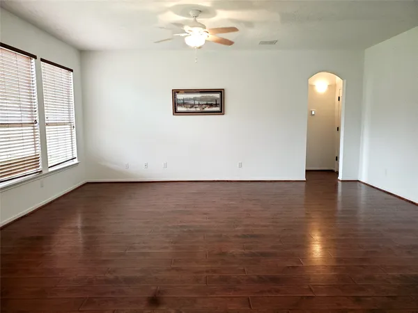 an empty room with wooden floor chandelier fan and windows