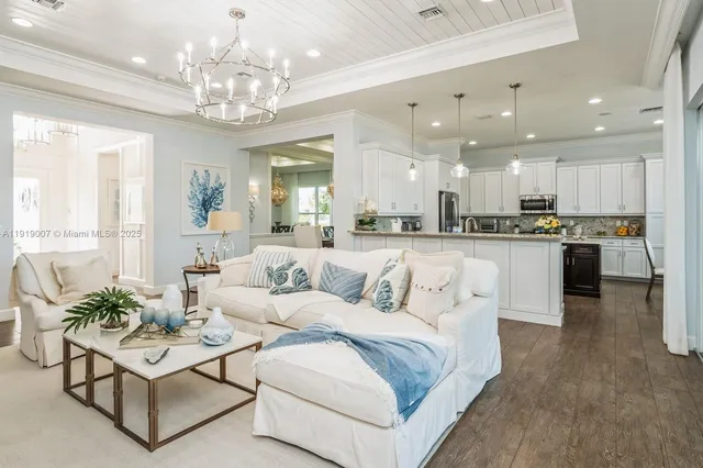 a large white kitchen with a chandelier and living room view
