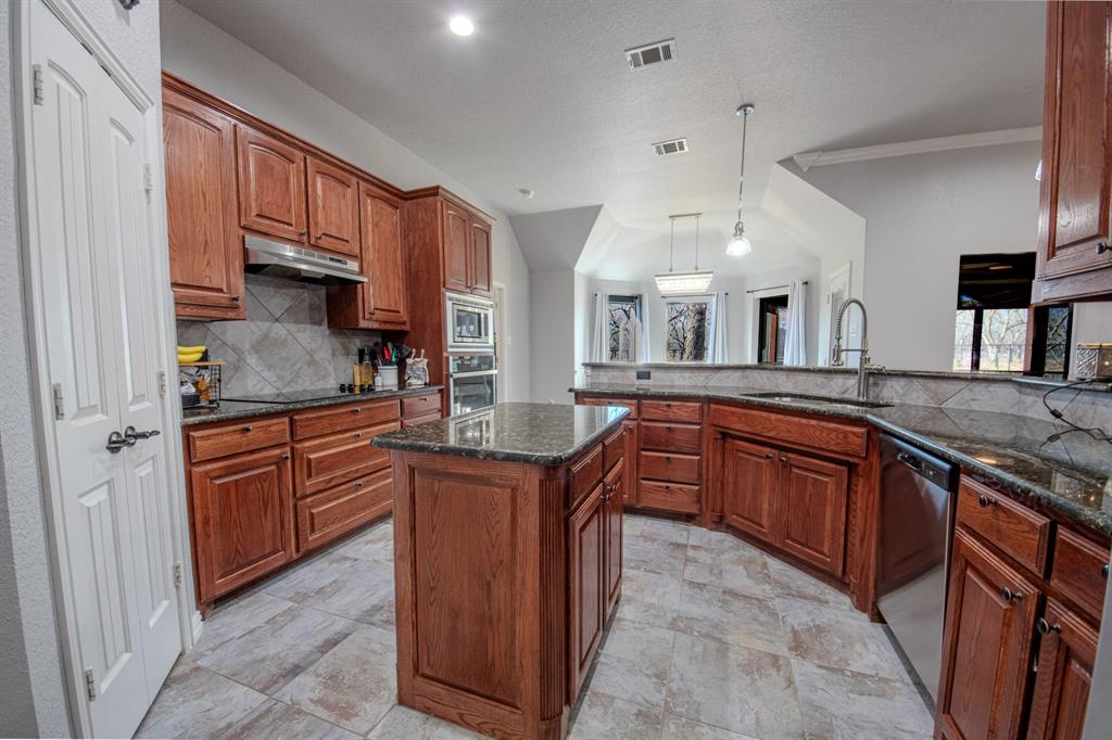 9001 Ravenswood Road Granbury, TX 76049 - Photo 16 of 38 Kitchen with tasteful backsplash, decorative light fixtures, dark stone counters, a center island, and crown molding