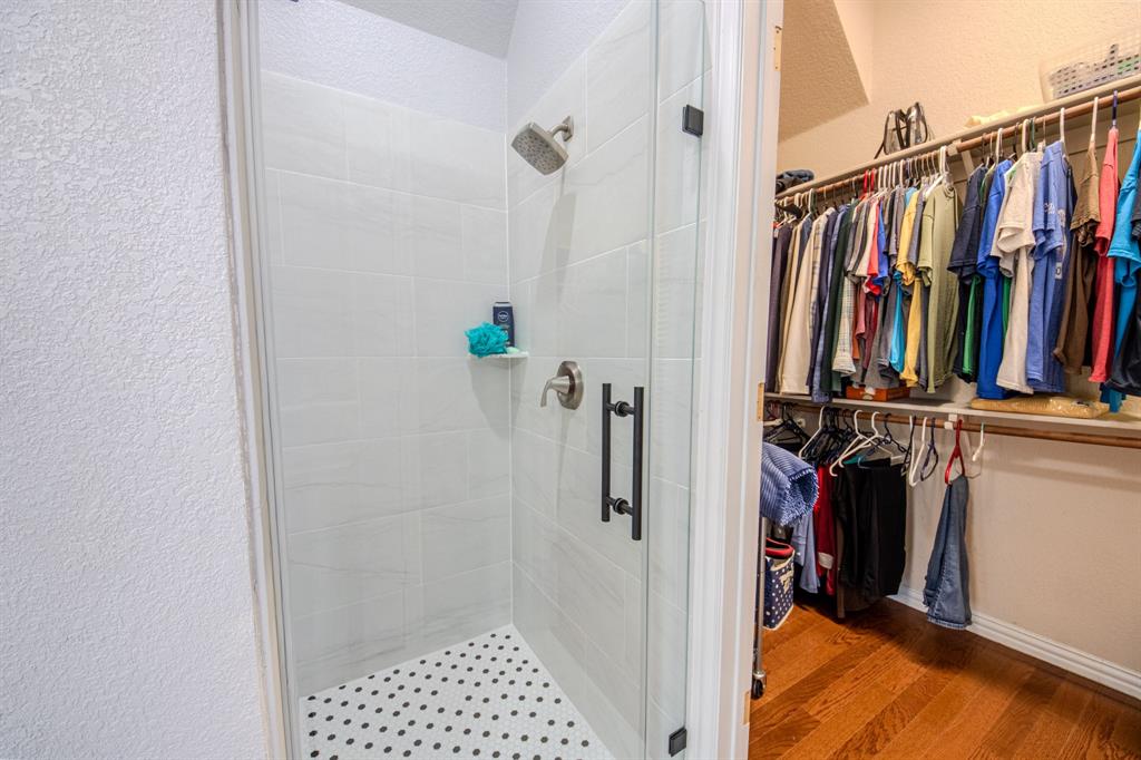 9001 Ravenswood Road Granbury, TX 76049 - Photo 24 of 38 Bathroom featuring a textured wall, a walk in closet, a shower stall, and light wood-type flooring