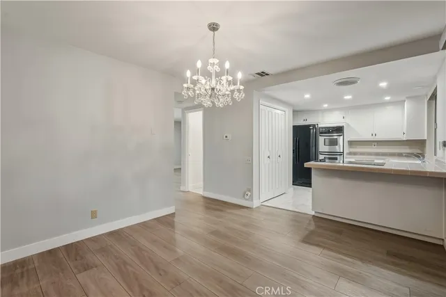 a view of a kitchen with granite countertop a refrigerator oven a sink dishwasher and white cabinets with wooden floor