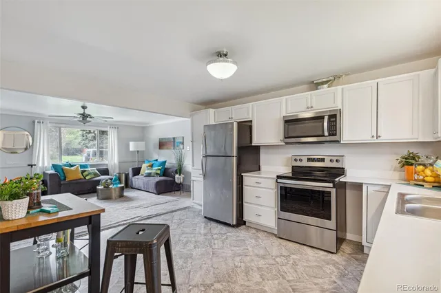 a living room with stainless steel appliances a stove a refrigerator a sink a stove a dining table and chairs with wooden floor