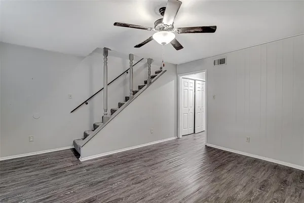 a view of an empty room with wooden floor and fan