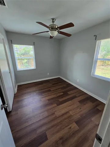 an empty room with wooden floor fan and windows