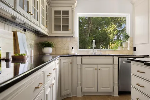 a kitchen with granite countertop a stove a sink and white cabinets with wooden floor
