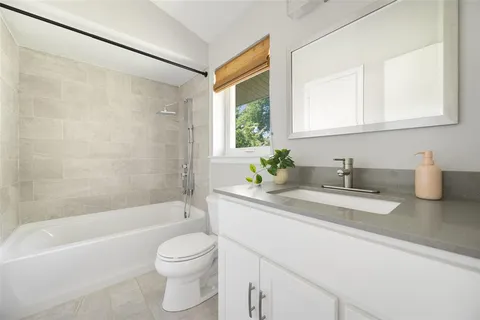 a bathroom with a granite countertop sink a toilet a mirror a bathtub and shower
