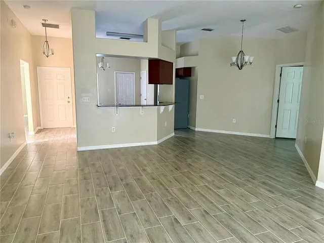 a view of a refrigerator in kitchen and an empty room with wooden floor