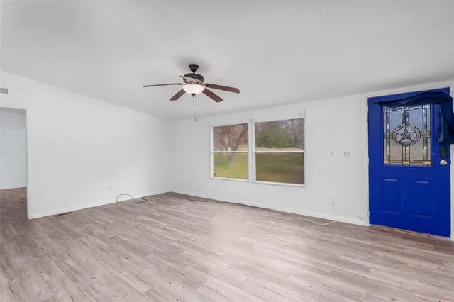 an empty room with wooden floor fan and windows