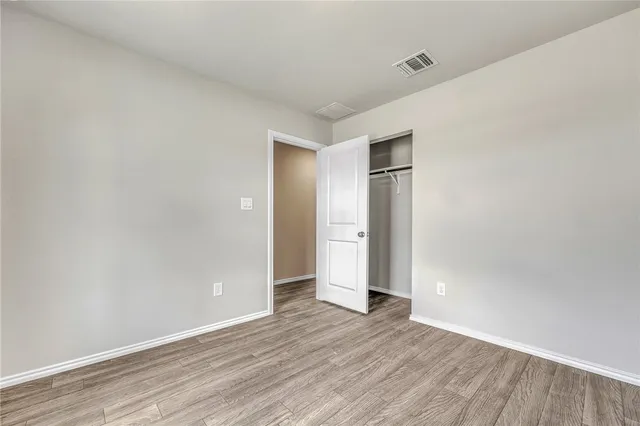 a view of an empty room with wooden floor and closet