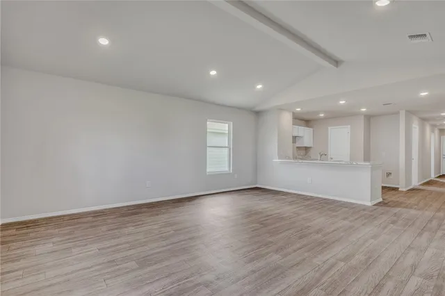 a view of an empty room with wooden floor and kitchen