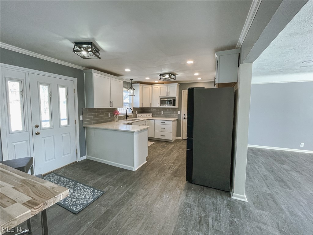 24709 Emery Road Warrensville Heights, OH 44128 - Photo 13 of 34 Kitchen featuring dark wood-type flooring, stainless steel microwave, tasteful backsplash, black refrigerator, and pendant lighting