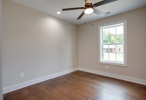 an empty room with wooden floor ceiling fan and windows
