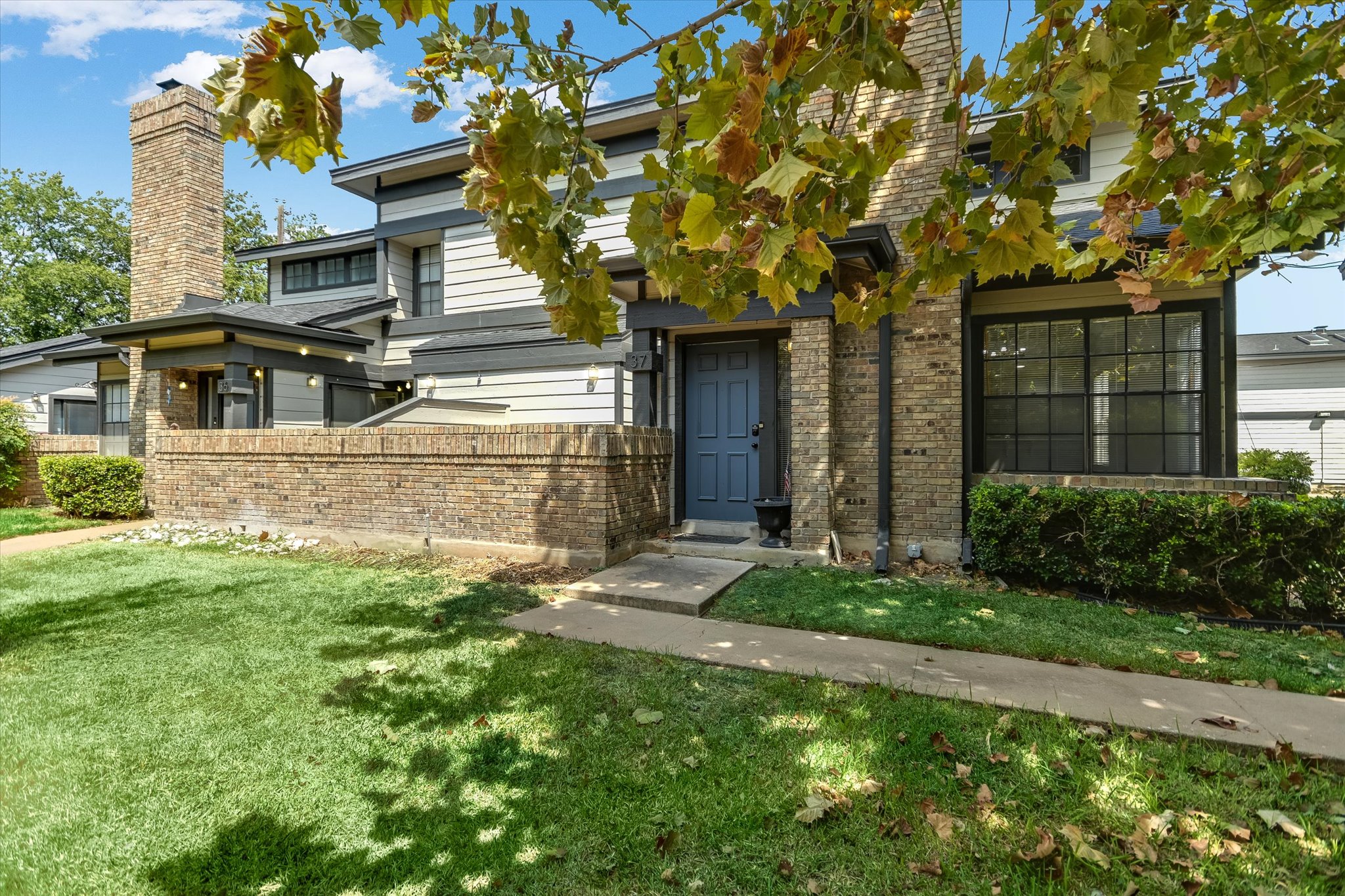 1748 Ohlen Road, Unit 37 Austin, TX 78757 - Photo 2 of 16 Mature trees shade a charming brick and siding exterior featuring a concrete walkway.