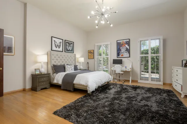 a spacious bedroom with a bed painting on wall and windows