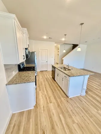 a large kitchen with kitchen island a stove a sink a refrigerator white cabinets and wooden floor