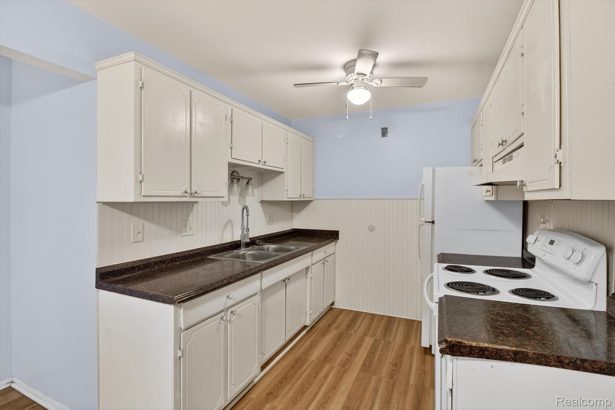 25301 Five Mile Road, Unit 109 Redford, MI 48239 - Photo 12 of 22 Kitchen featuring white range with electric stovetop, dark countertops, light wood-style floors, white cabinetry, and a wainscoted wall