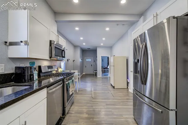 a kitchen with stainless steel appliances granite countertop a refrigerator a stove a sink a refrigerator and white cabinets with wooden floor