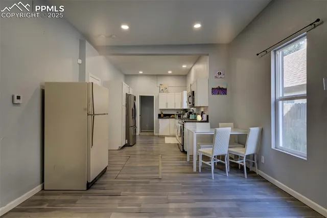 a dining area with stainless steel appliances granite countertop a refrigerator a sink dishwasher a dining table and chairs with wooden floor