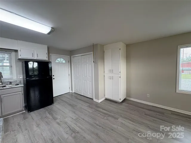 an empty room with wooden floor kitchen view and a window