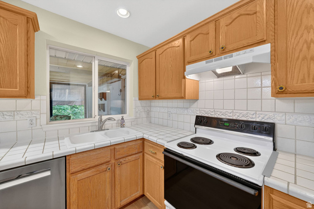 1464 990 West Provo, UT 84601 - Photo 15 of 41 Kitchen featuring wood cabinetry, tile countertops, tile backsplash, stainless-steel sink, and a white electric range with a range hood