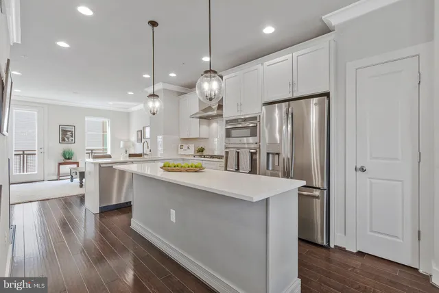 a kitchen with stainless steel appliances kitchen island a refrigerator a sink dishwasher a oven and a dining table with wooden floor