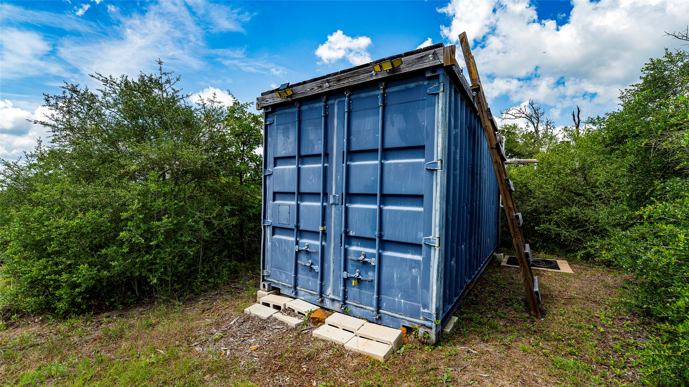 1470 22 Hills Road Gause, TX 77857 - Photo 16 of 35 A robust storage container rests amidst natural foliage, providing essential utility for the property.