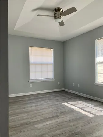 an empty room with wooden floor chandelier fan and windows