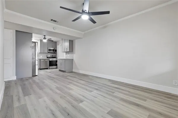 an empty room with wooden floor kitchen view and a refrigerator