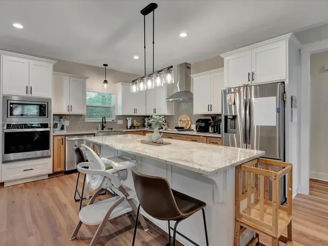 a kitchen with stainless steel appliances granite countertop a sink a stove a refrigerator cabinets and chairs