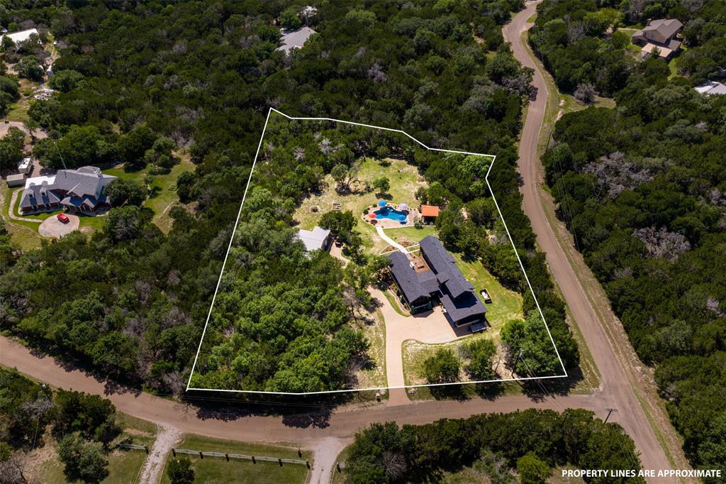 124 Bluffview Circle China Spring, TX 76633 - Photo 5 of 40 Expansive property featuring a dark-toned residential structure, a detached guest house, a visible swimming pool, a driveway, and extensive surrounding tree cover