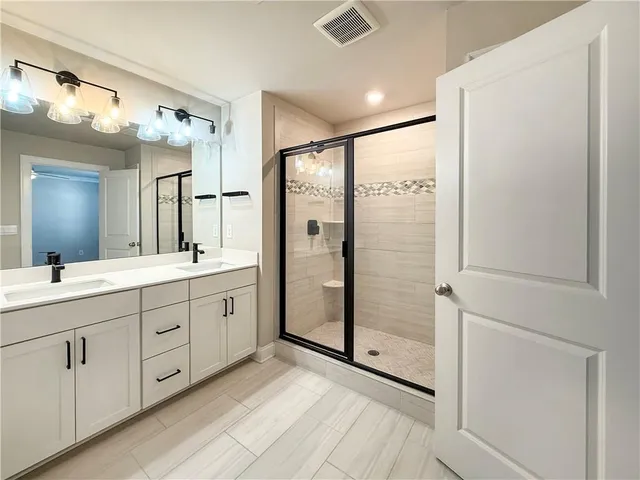 a spacious bathroom with a double vanity sink a large mirror a shower and vanity