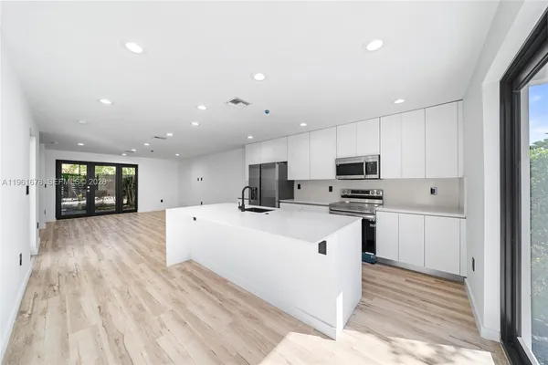 a large white kitchen with kitchen island a sink a center island stainless steel appliances and a window