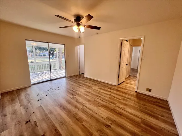 an empty room with wooden floor chandelier fan and windows