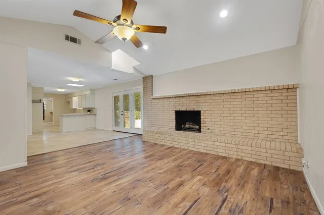 a view of an empty room with wooden floor a ceiling fan and a kitchen view