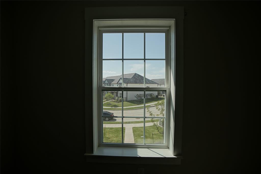1764 Palladio Loop Princeton, TX 75407 - Photo 40 of 40 Vertical window with white trim and muntins, showcasing a neighborhood street, green lawns, and residential structures under a clear sky