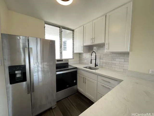 a kitchen with stainless steel appliances granite countertop a refrigerator a sink a stove and white cabinets