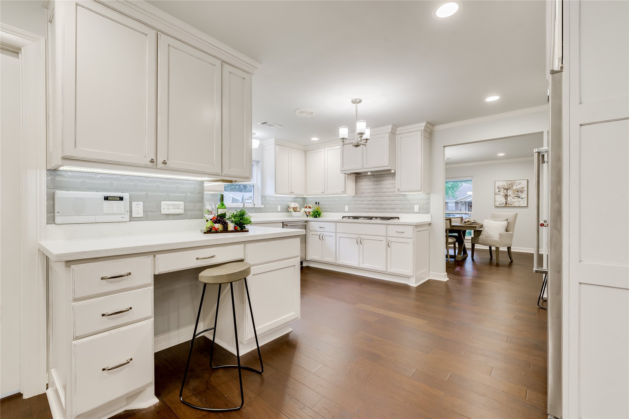 1010 Thornton Road Houston, TX 77018 - Photo 10 of 27 This kitchen features elegant white cabinetry, stainless steel appliances, and a desk with seating. The open layout flows into a bright dining area, all set on rich engineered hardwood floors. Modern lighting and ample counter space enhance the functional yet stylish design.