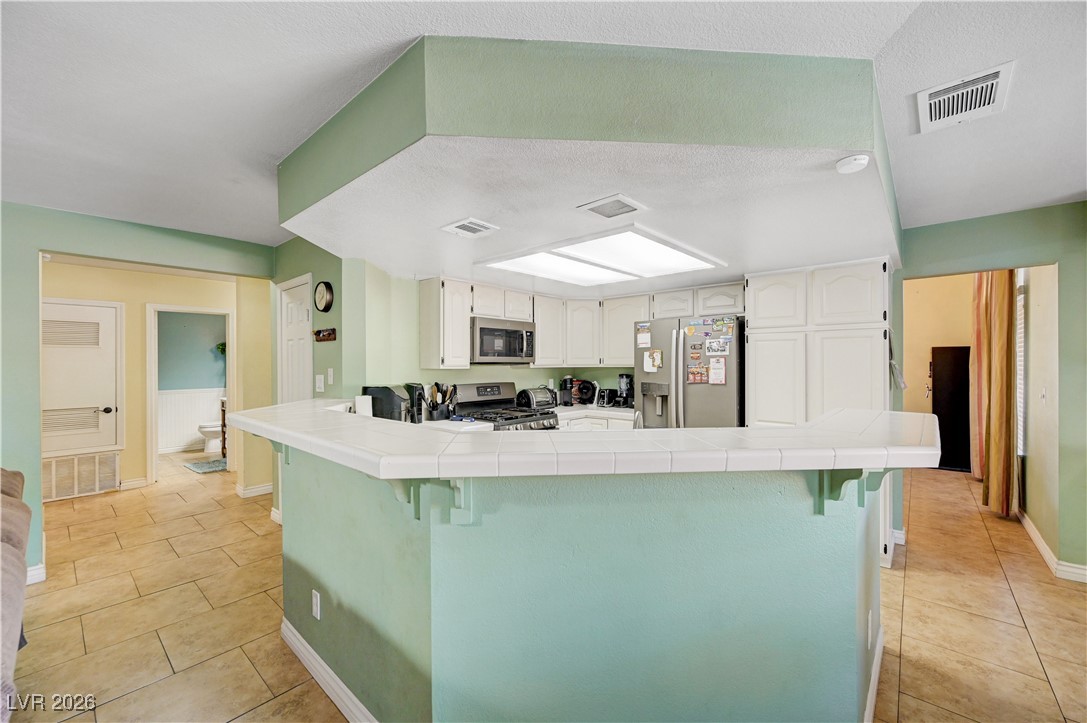 14 Barton Spring Circle Henderson, NV 89074 - Photo 11 of 64 Kitchen featuring tile counters, white cabinets, a kitchen bar, and appliances with stainless steel finishes