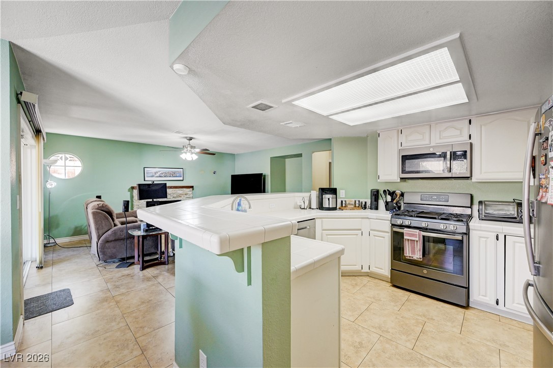 14 Barton Spring Circle Henderson, NV 89074 - Photo 63 of 64 Kitchen with tile counters, stainless steel appliances, white cabinets, open floor plan, and a peninsula