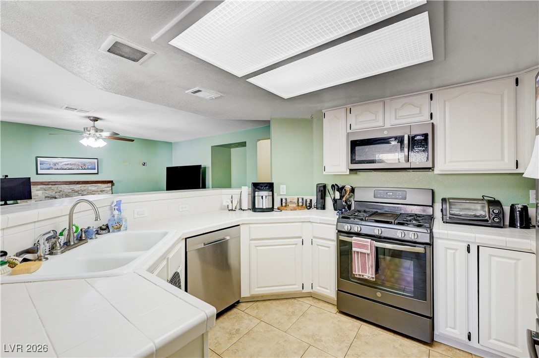 14 Barton Spring Circle Henderson, NV 89074 - Photo 12 of 64 Kitchen with tile countertops, stainless steel appliances, white cabinetry, light tile patterned floors, and a textured ceiling
